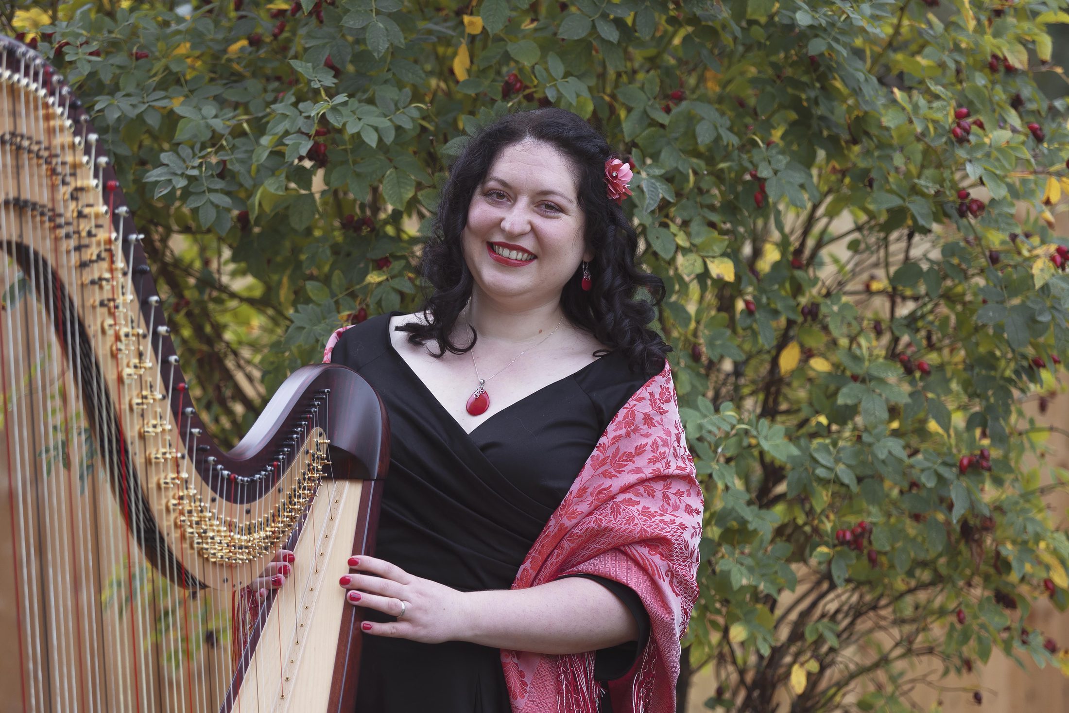 Maria Trotter smiling beside her harp in a garden