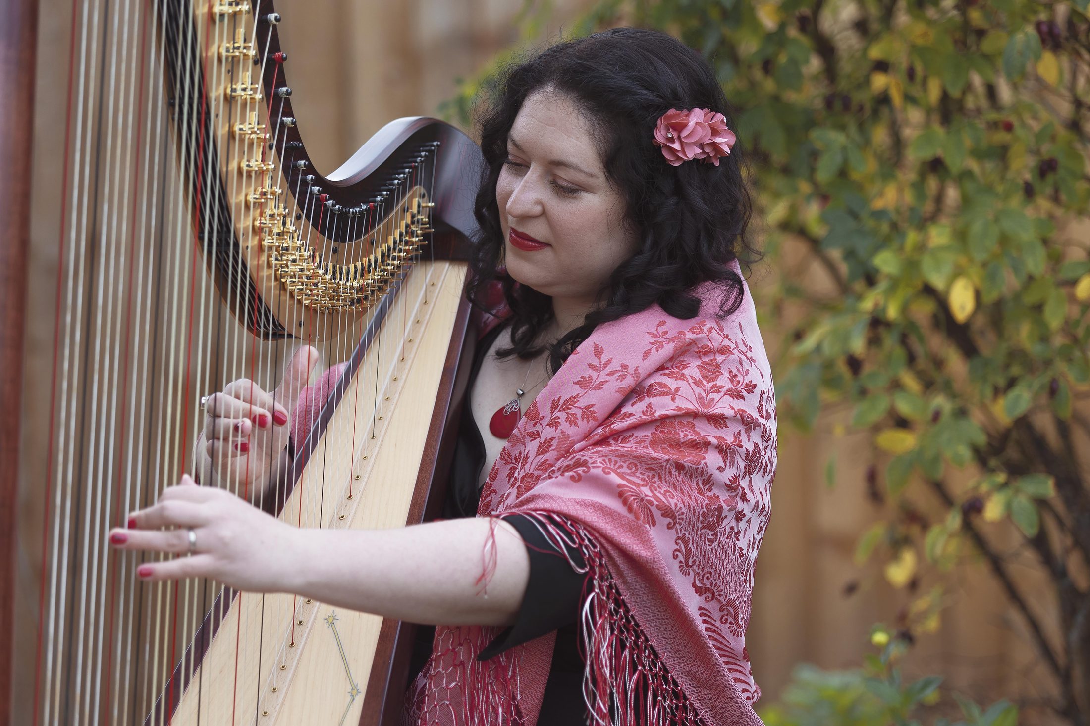Maria playing harp outdoors among garden foliage